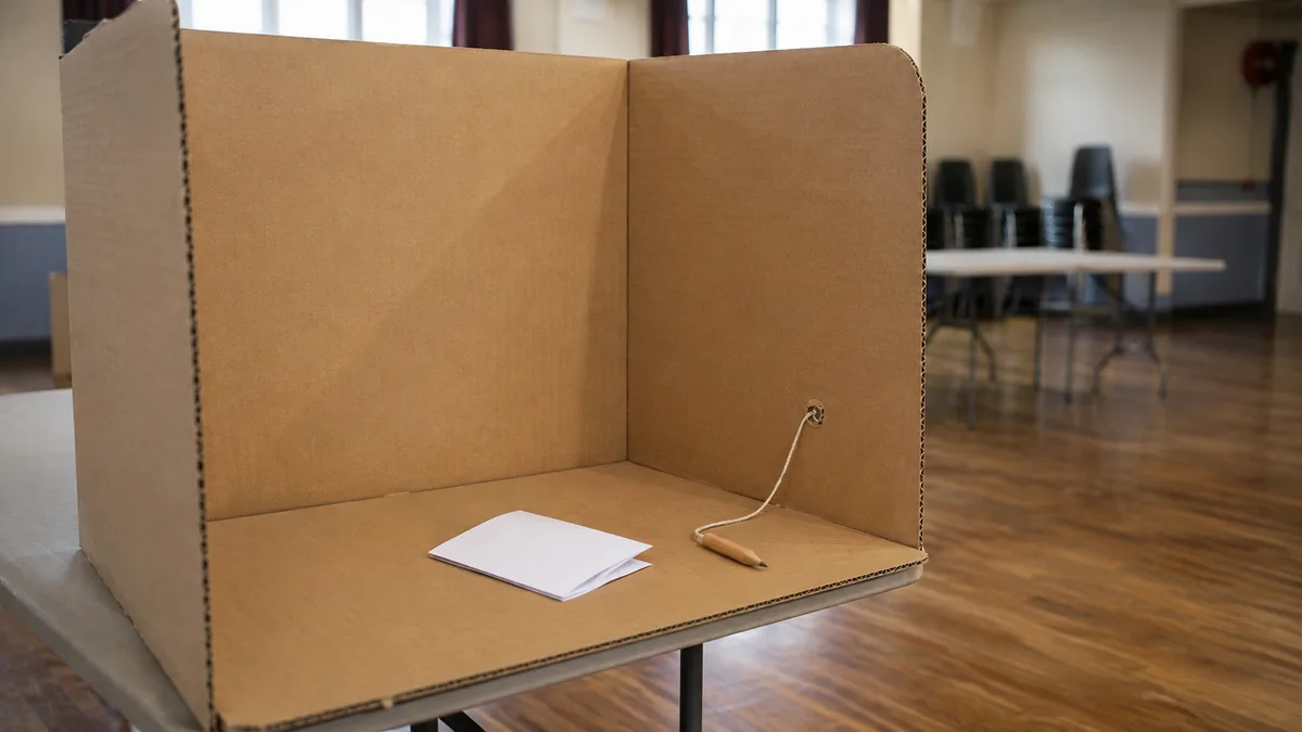 A voter slides a folded paper ballot into a cardboard Elections Canada ballot box